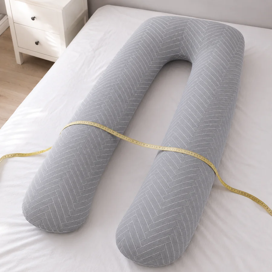 A soft tape measure laid across the U-shaped pregnancy pillow on a bed